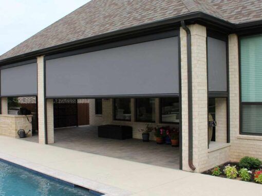 A brick home with white rolling shutters installed on the front windows.